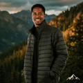 Man wearing a dark puffer jacket standing in front of a mountainous landscape with trees.